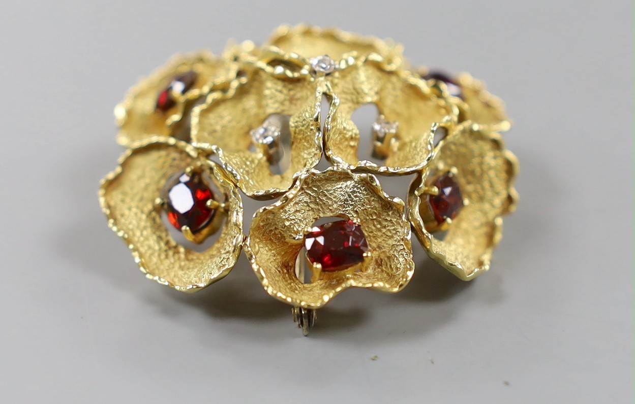 A 1960's textured 18ct gold, garnet and diamond cluster set open work flower head brooch, maker C.V.E over W., London, 1966, 44mm, gross weight, 19.2 grams.